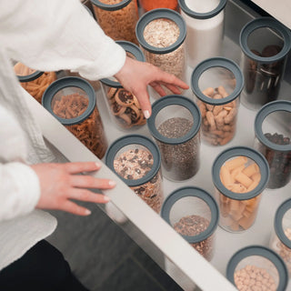 Blick von oben in eine perfekt organisierte Küchenschublade; eine Hand greift nach einem 1000ml Pure Glas inmitten von Pasta, Linsen und Saaten.