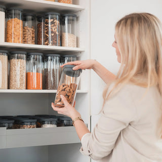 Frau entnimmt Schokokekse aus einem 1000ml Vorratsglas vor einem perfekt sortierten Vorratsschrank; zeigt die visuelle Ruhe und Ordnung des Systems.